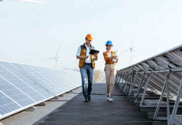 View on the rooftop solar power plant with two engineers walking and examining photovoltaic panels. Concept of alternative energy and its service