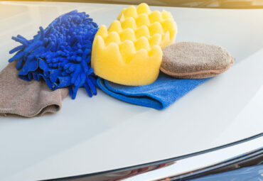 Yellow, green sponges and blue mitts for washing and microfiber fabric with cleaner cloth on white car