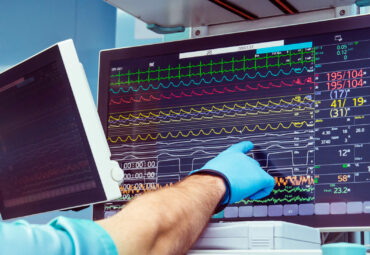 Male anaesthesiologist hand pointing vital activity data at modern monitor system in operation room. Selective focus