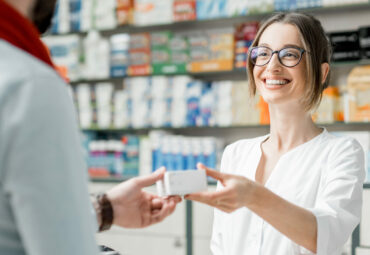 Young woman pharmacist giving medications to the male client standing at the paydesk of the pharmacy store