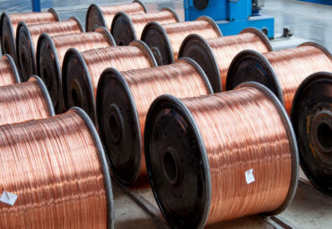 Several rows of new finished coils with copper wire in the production shop. Copper wire is wound on metal coils or drums. Modern line of automatic production of electric cable and wire.