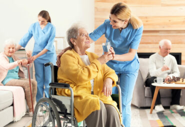 Nurse giving glass of water to elderly woman in wheelchair at retirement home. Assisting senior people