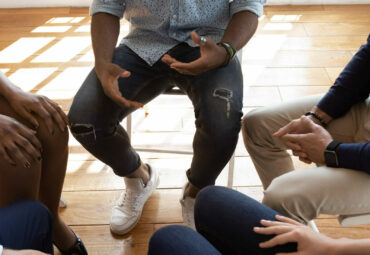 Close up top view unrecognizable multiracial workers strategizing indoors at informal atmosphere, people seated in circle talking share problems tell stories during psychological rehab session concept