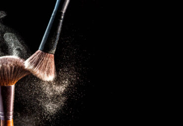 Make up cosmetic brushes with powder blush explosion on black background. Skin care or fashion concept. Free space for your text.