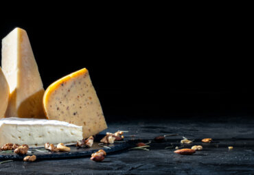 Different kinds of cheese with nuts on dark background, copy space