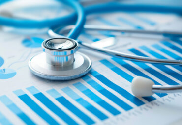 Close-up image of a stethoscope on detailed bar graph charts, suggesting in-depth healthcare research and data analysis